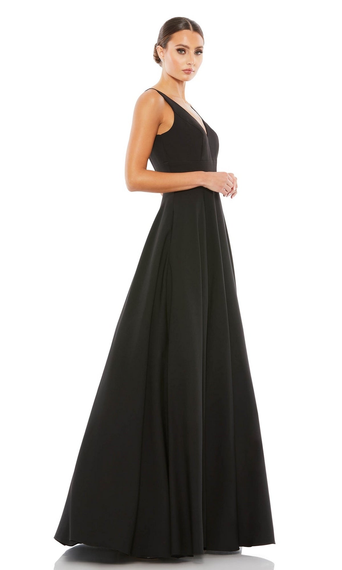 Woman in the Mac Duggal 48924 Classic Long Prom Ball Gown, a sleeveless black floor-length dress, stands facing left with hands clasped against a plain white background.
